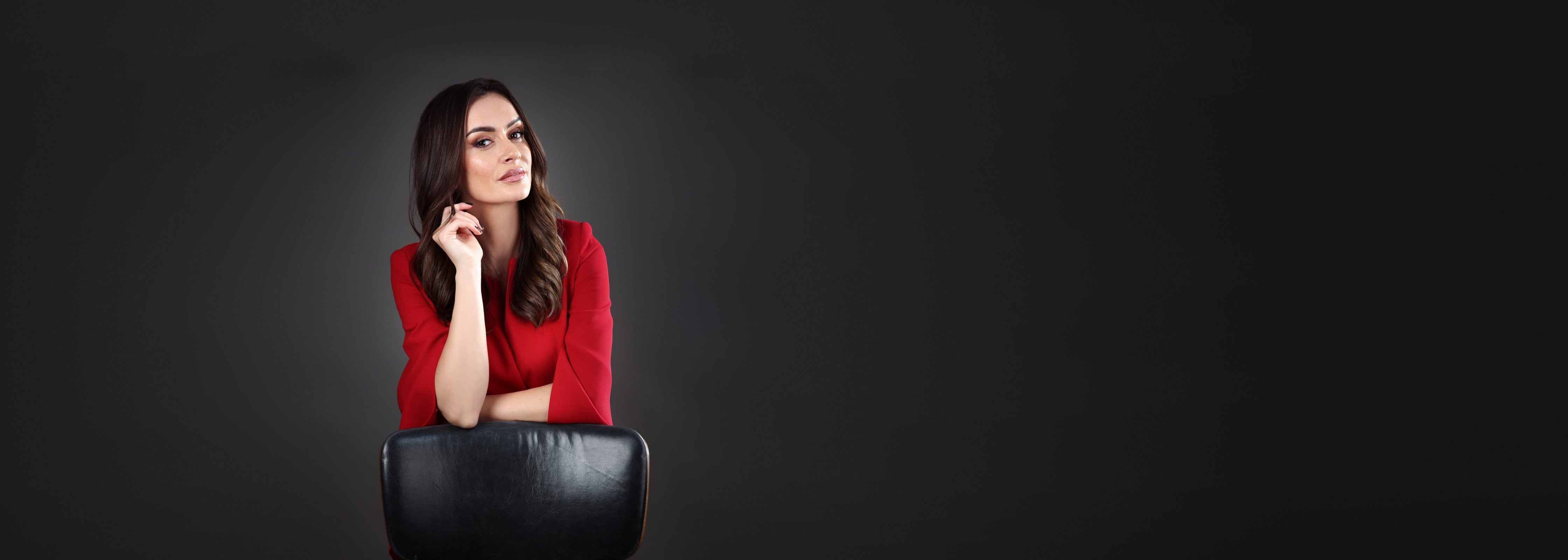 Mia Pavlikova in a red blouse, leaning on the back of a studio chair