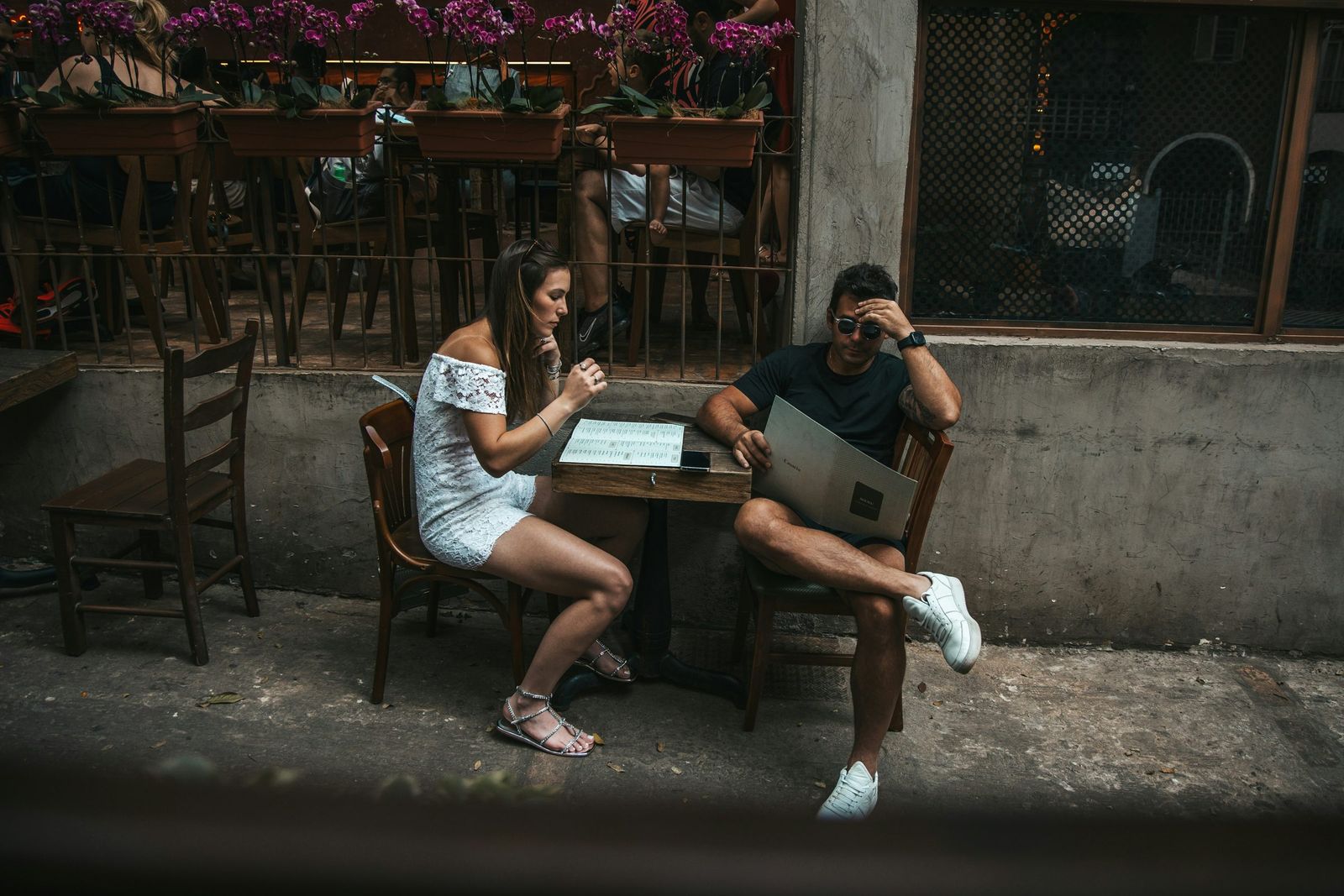 A couple at a café table, laughing over a laptop and a phone